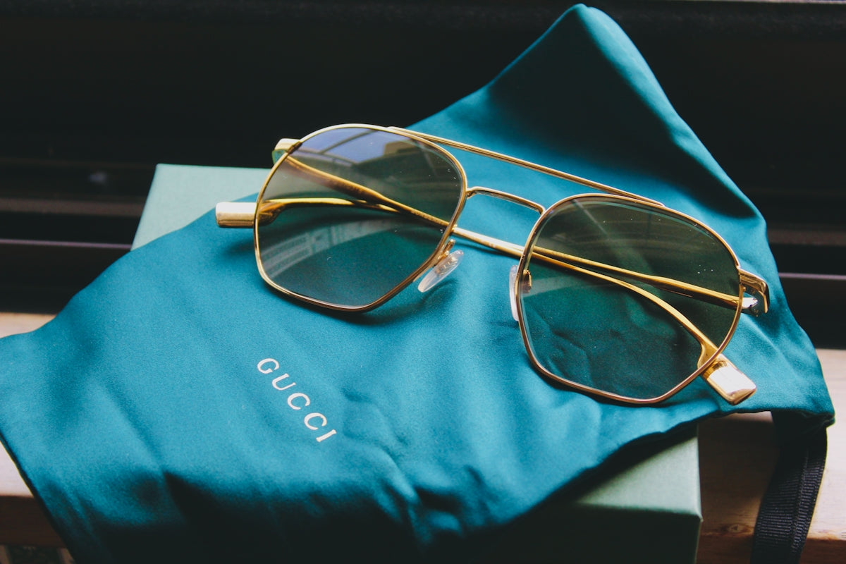 Gold framed aviator sunglasses on a teal cloth.