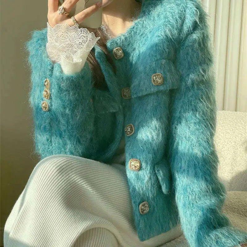 Close-up of a turquoise textured jacket with decorative gold-tone buttons, white lace cuffs and an ivory ribbed skirt.