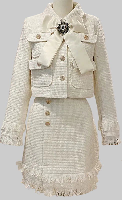 White tweed suit with a large bow and brooch on a mannequin against a gray background