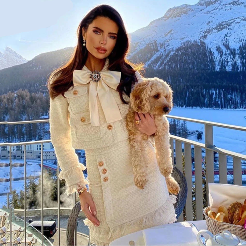 Woman in a stylish outfit holding a dog with a snowy mountain landscape in the background