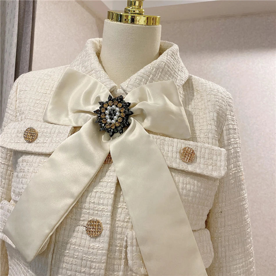 White textured coat with a large bow and decorative brooch on a mannequin.