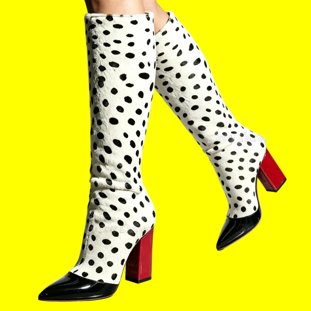 A pair of knee-high boots with a white faux-hair dalmatian spot pattern, black pointed toes, and bright red block heels, shown on a model's legs against a white studio background.