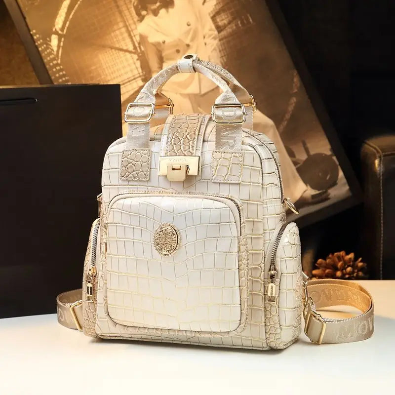 White crocodile-patterned backpack with gold accents on a blurred background