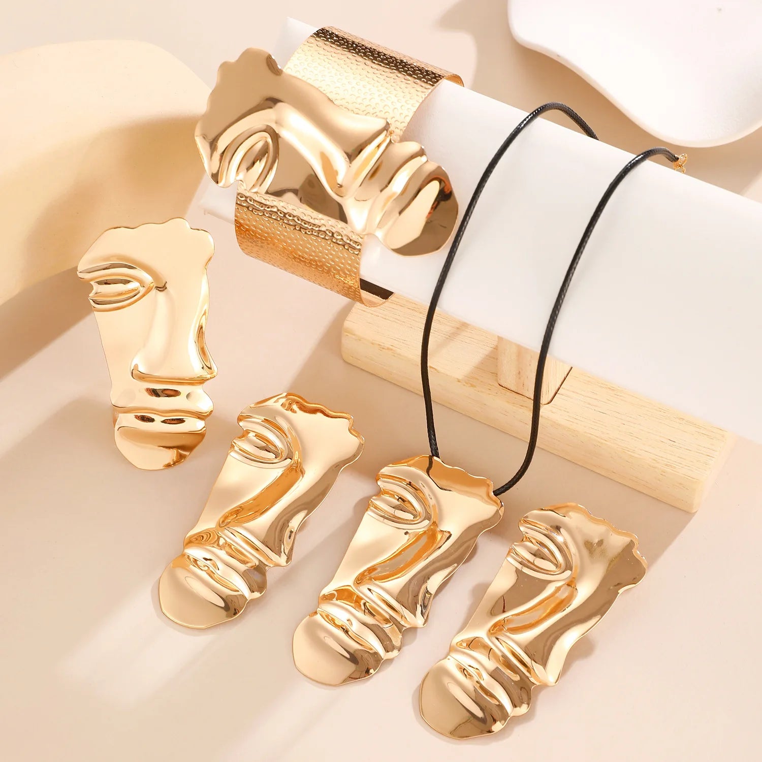 Gold face-shaped jewelry pieces on a light background