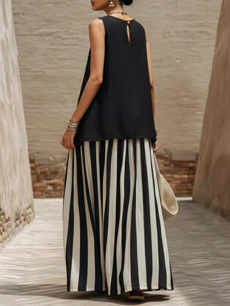 Woman wearing a black sleeveless top and black and white striped pants, standing in a sunlit outdoor setting.