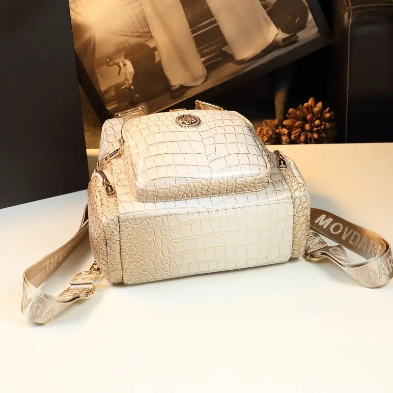 Beige crocodile-patterned handbag with a visible brand logo on a white surface.