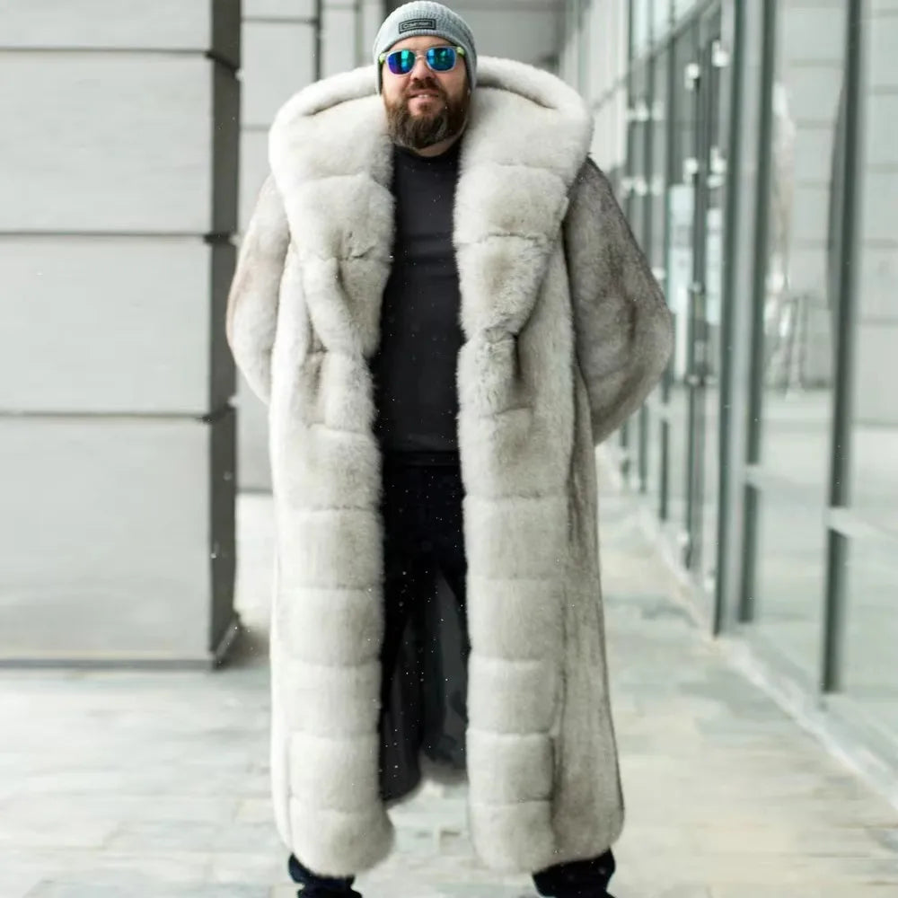 A man wearing a long, plush light gray fur coat over a black outfit, standing outdoors in front of a modern glass building.