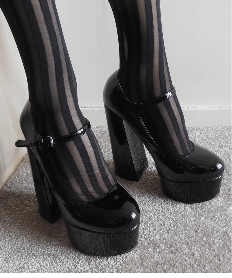 Black patent leather platform high heels with ankle straps, shown worn with black-and-gray striped tights on a carpeted floor.