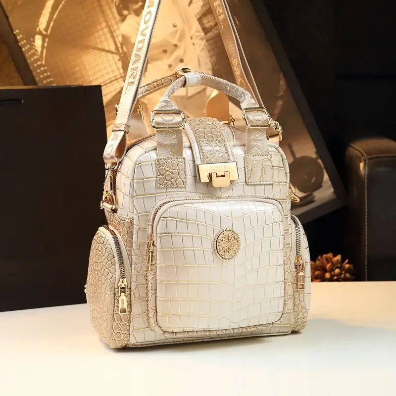 Beige crocodile-patterned handbag with gold accents on a blurred background