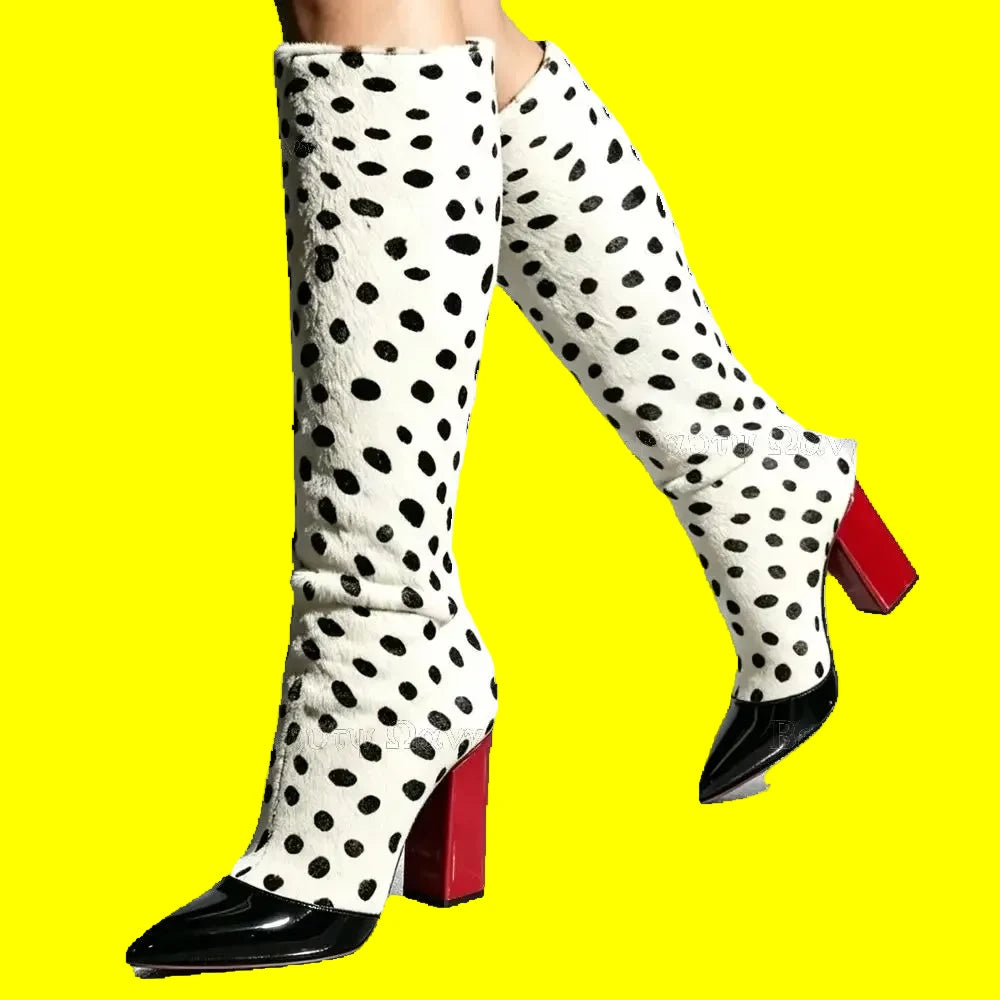 A pair of knee-high boots with a white faux-fur texture covered in black spots, featuring glossy dark red pointed toes and block heels, shown on a model against a light gray background.