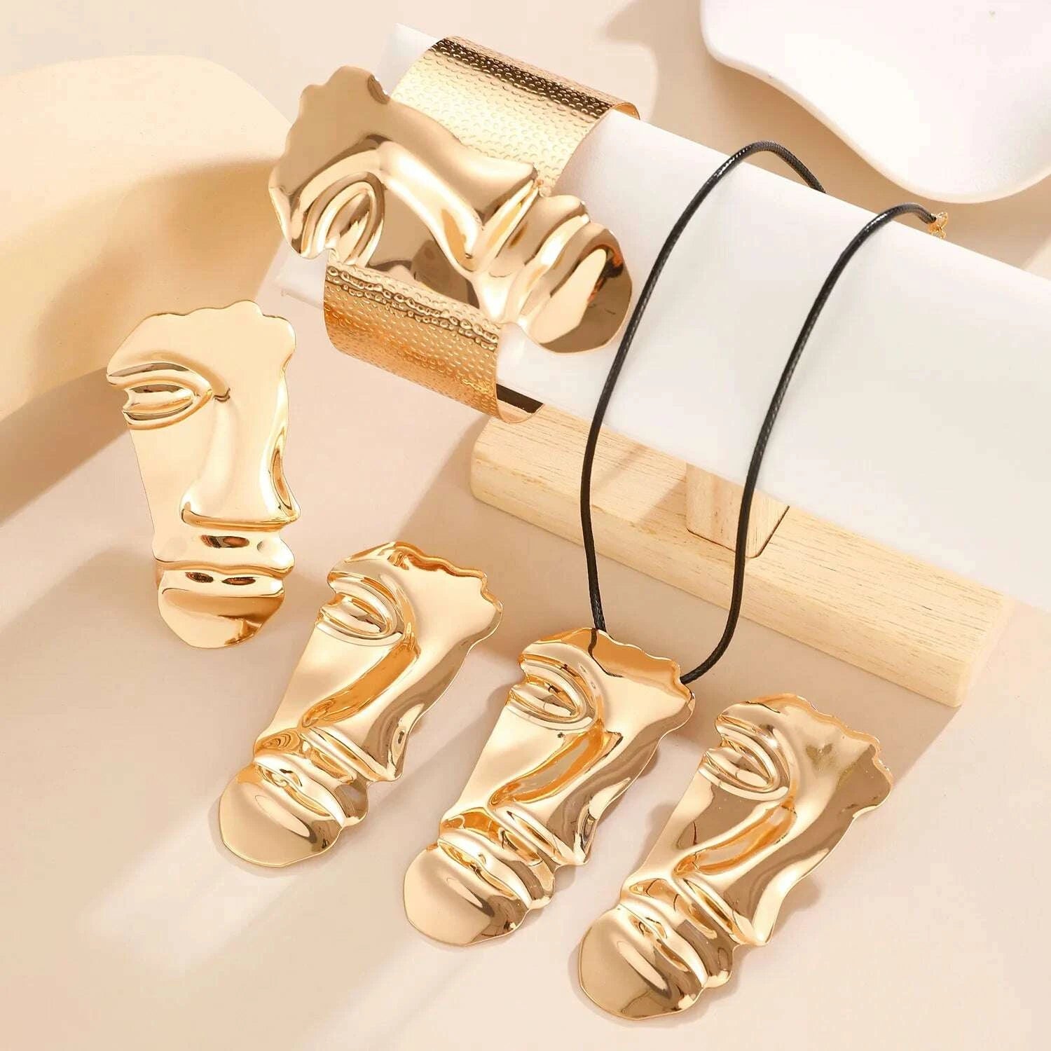 Gold face-shaped jewelry pieces on a light background