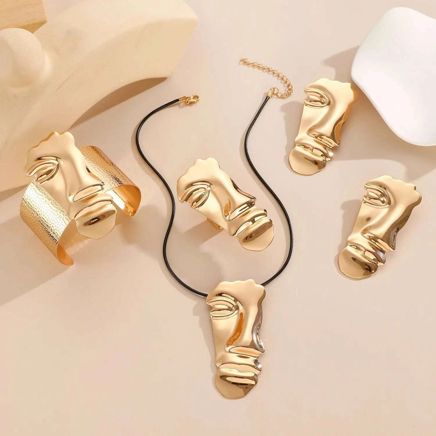 Gold jewelry with face designs on a beige background