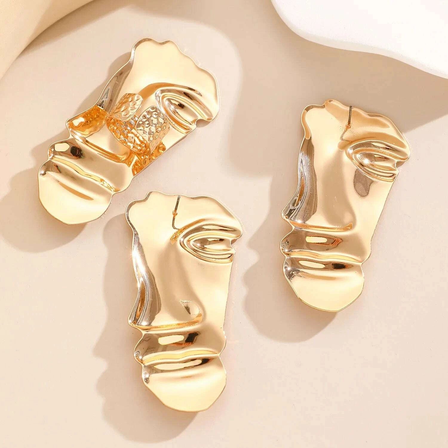 Gold face-shaped earrings on a beige background
