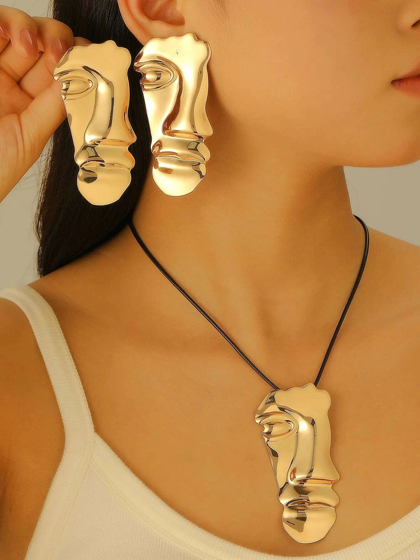 Gold face-shaped earrings and necklace on a model against a neutral background