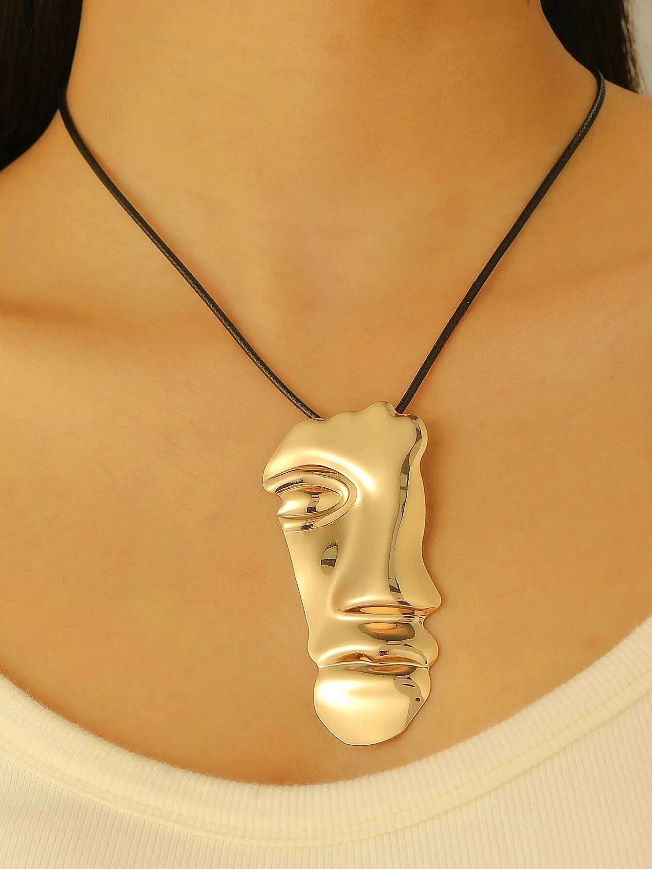 Gold face-shaped pendant on a black cord worn by a person