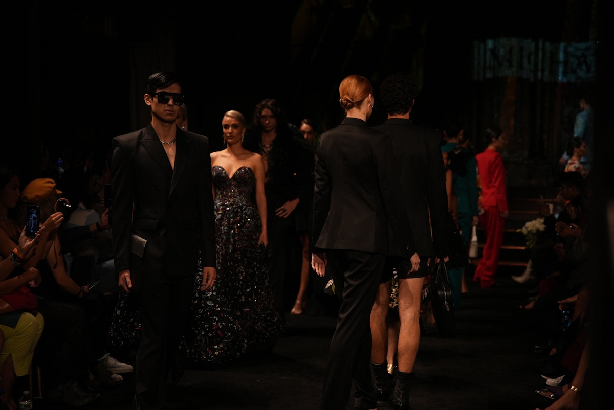 Fashion models parade on a dimly lit runway.