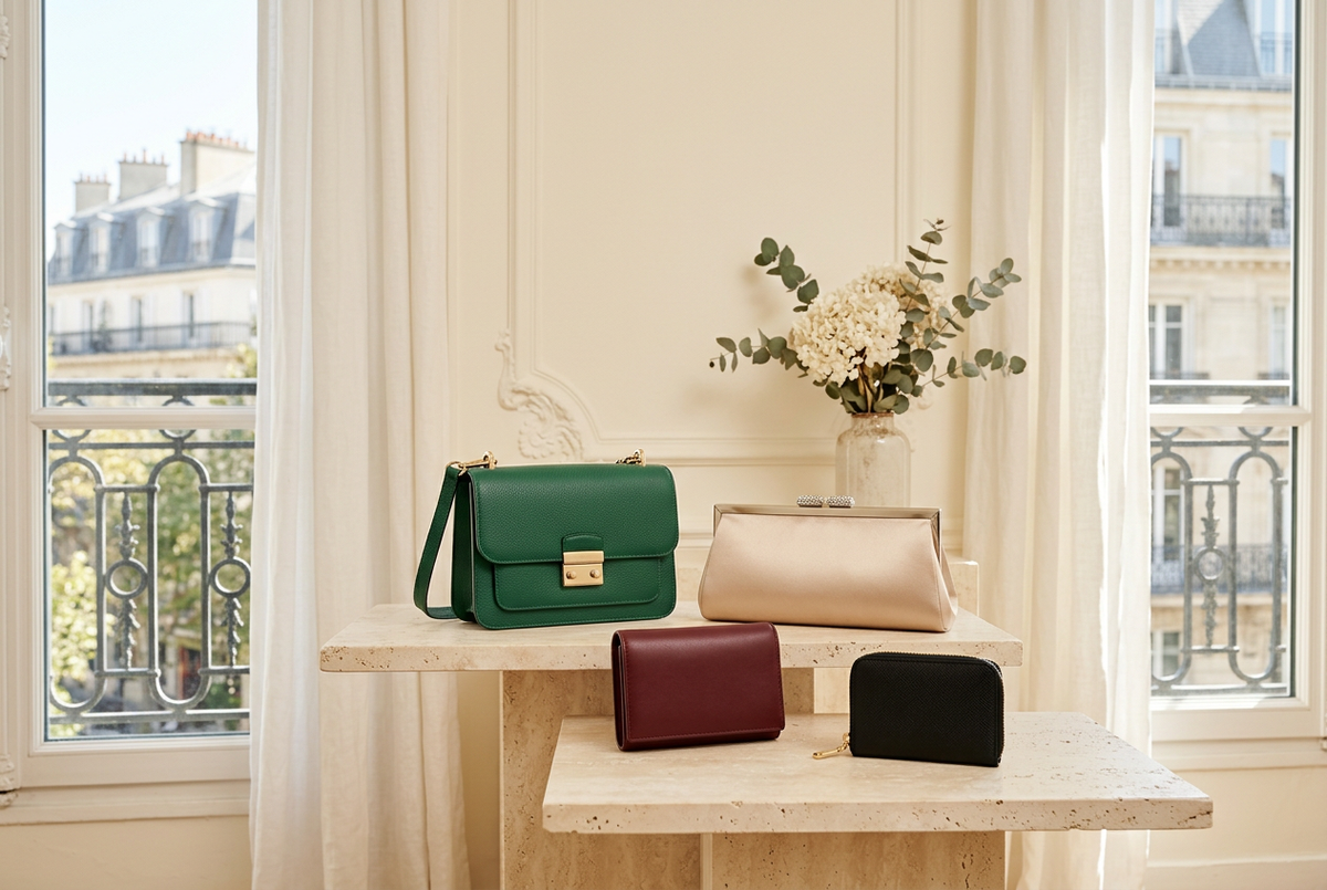 Emerald shoulder purse, champagne evening clutch, burgundy wallet and black coin purse arranged on pale stone in soft daylight.