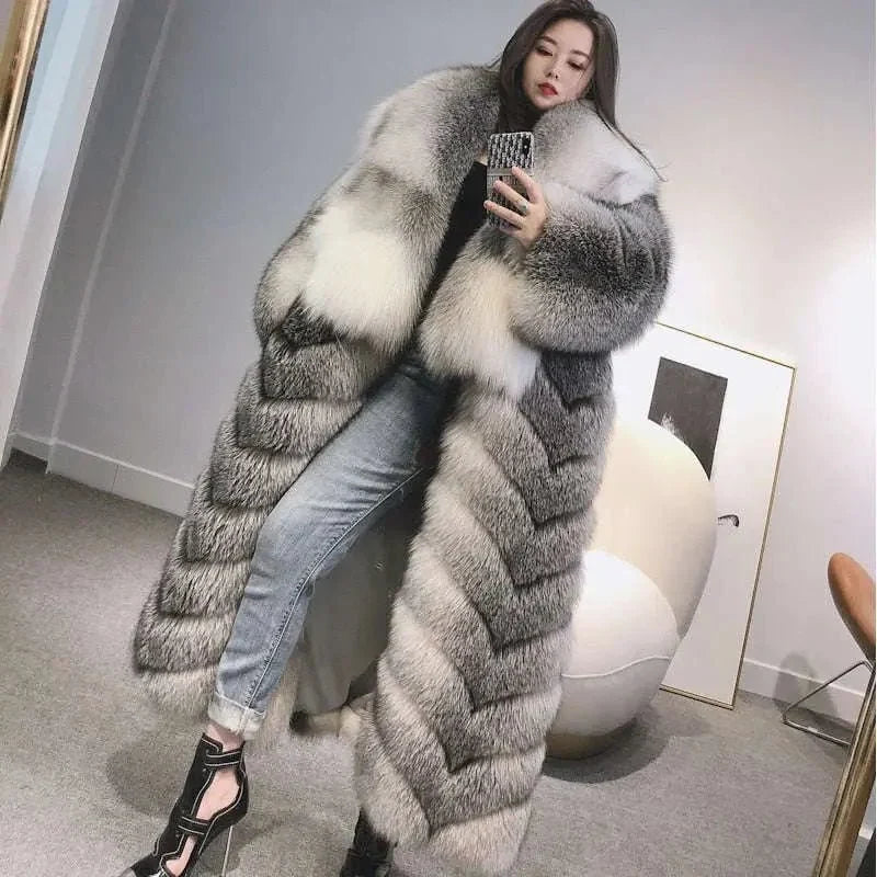 Woman taking a mirror selfie in a long grey and cream fur-textured coat, jeans and black heels.