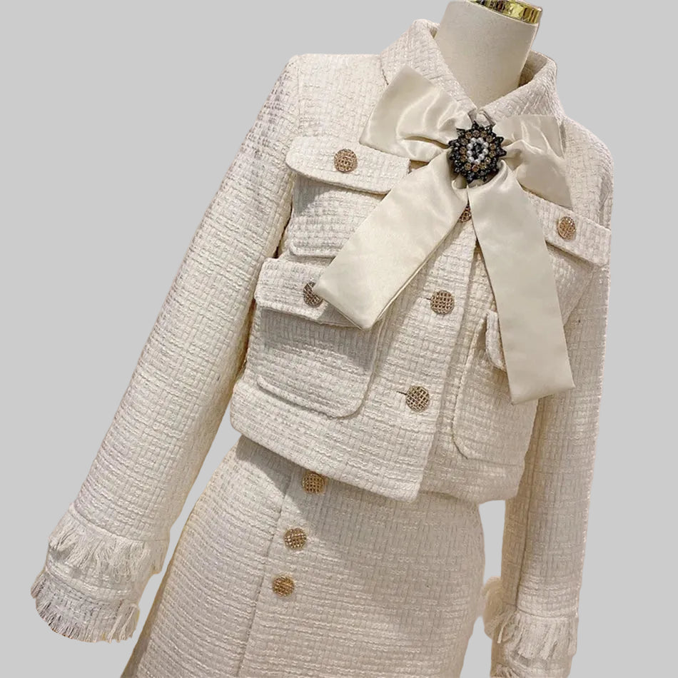 Beige tweed suit with a large bow and brooch on a mannequin against a gray background