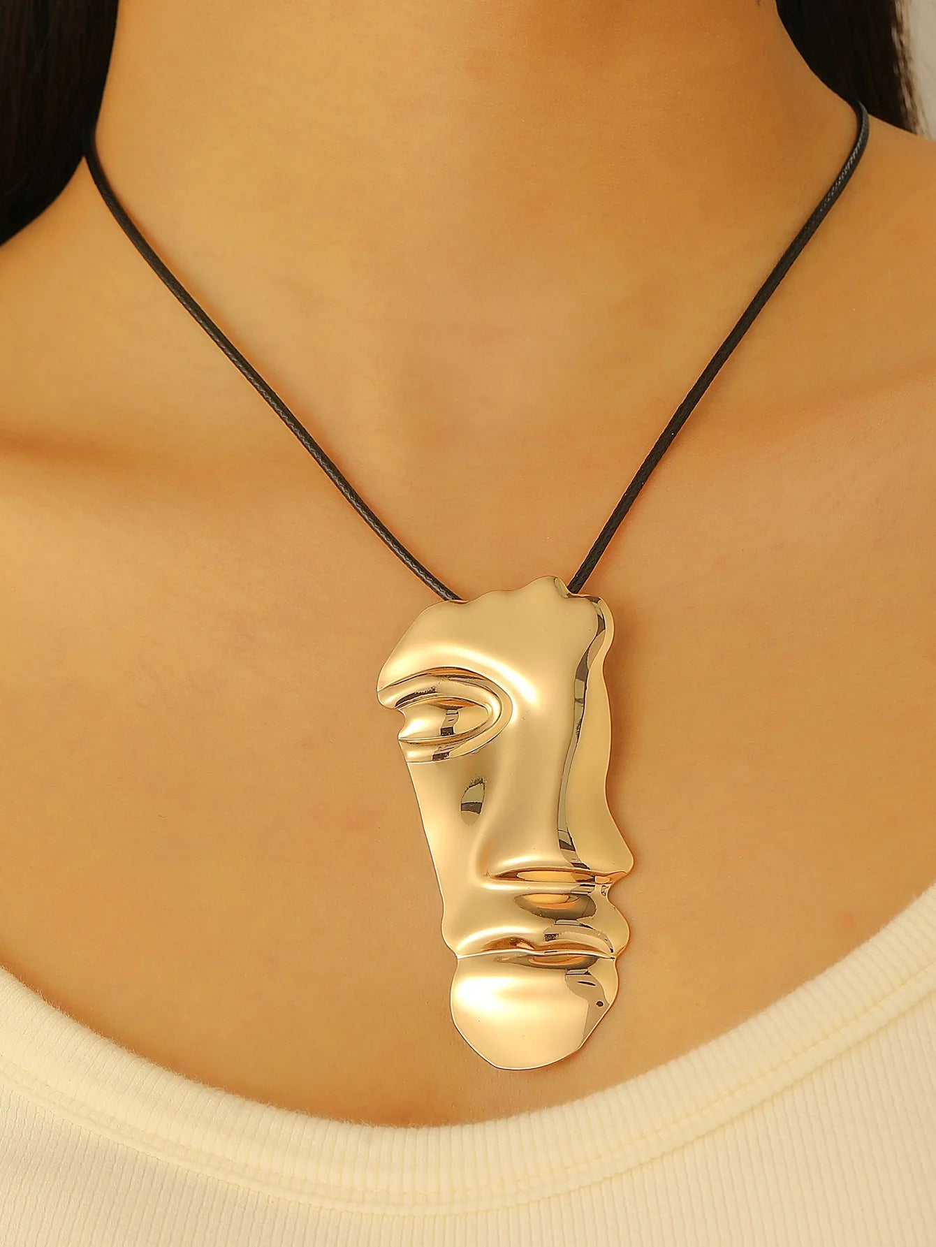 Gold face-shaped pendant on a black cord worn by a person