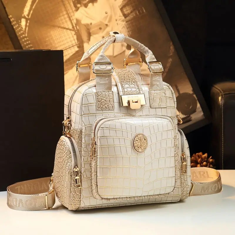 Beige crocodile-patterned handbag with gold accents on a light surface.