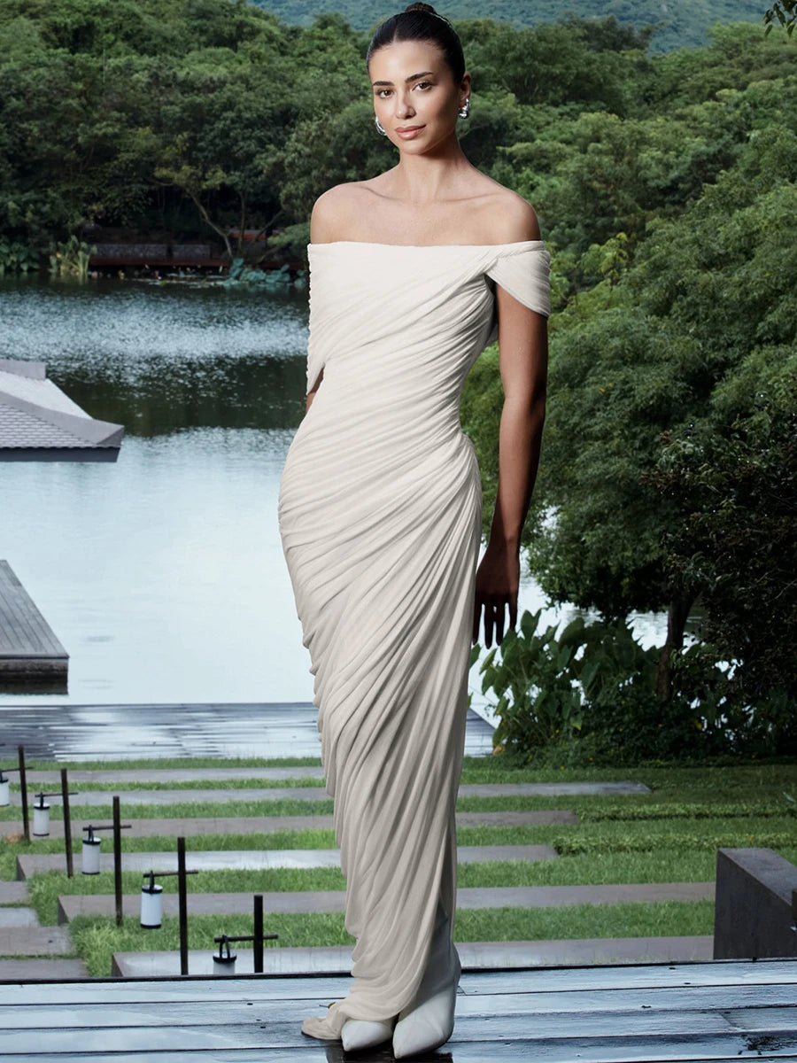 Woman in a white off-shoulder gown standing outdoors by a lake