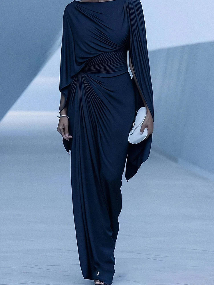 Navy blue draped dress worn by a model on a runway.
