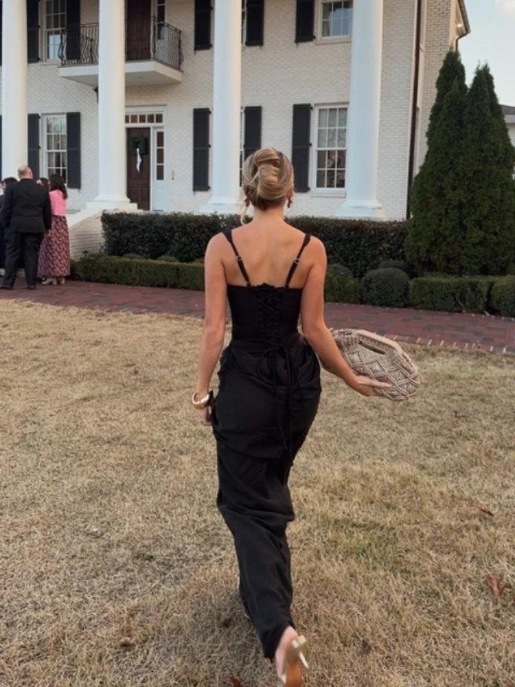 Woman in a black dress walking on grass in front of a large white house.
