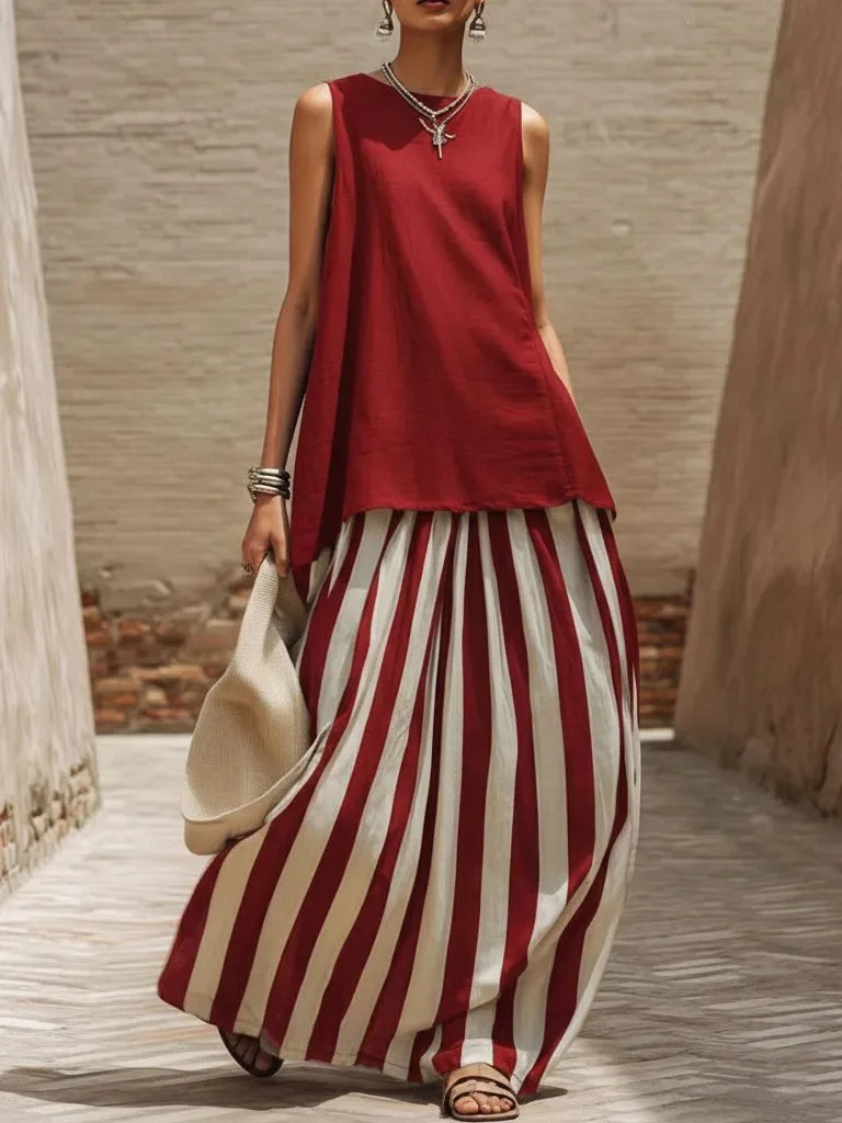 Woman wearing a red sleeveless top and red and white striped pants, holding a beige hat.
