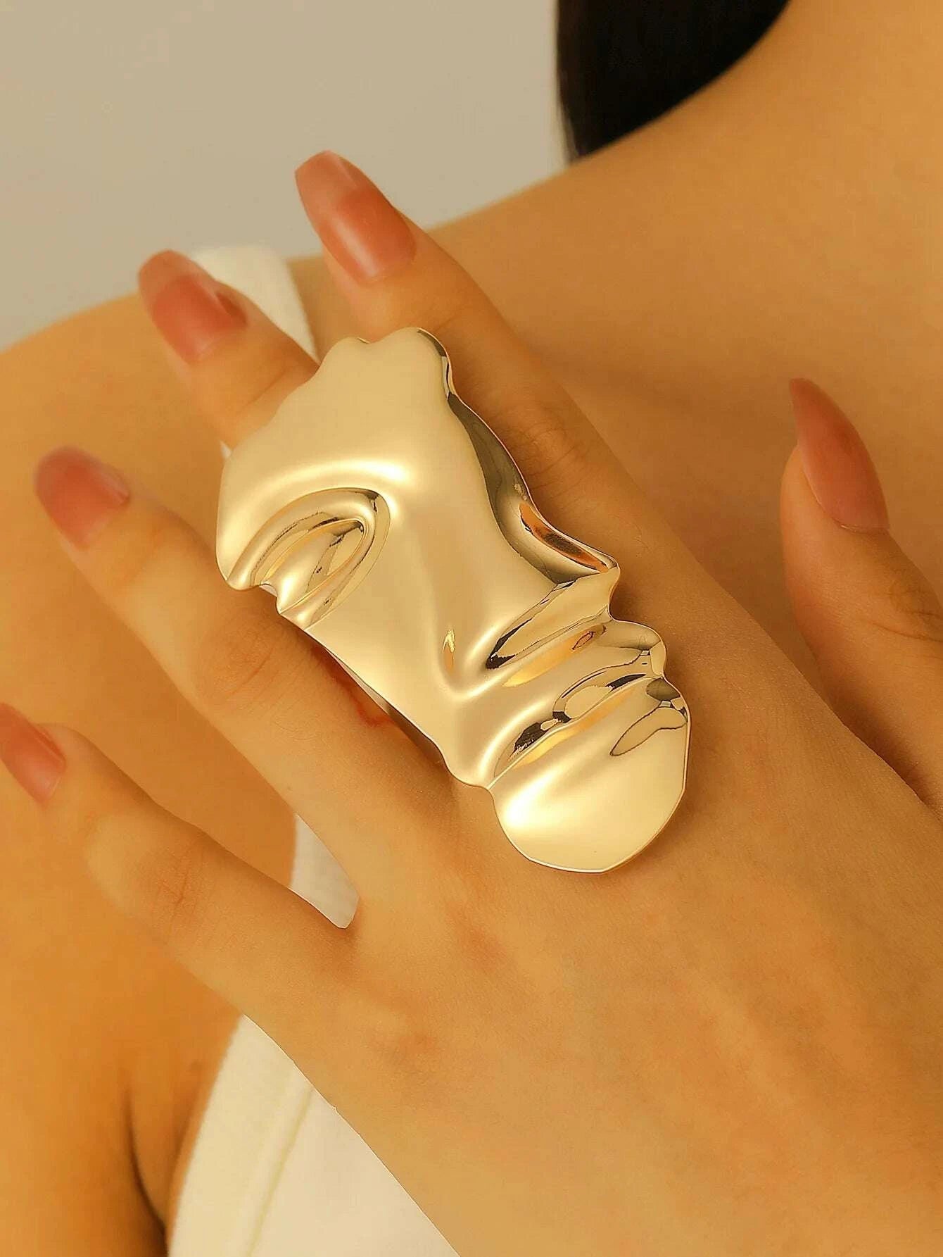 Gold face-shaped ring on a hand against a neutral background