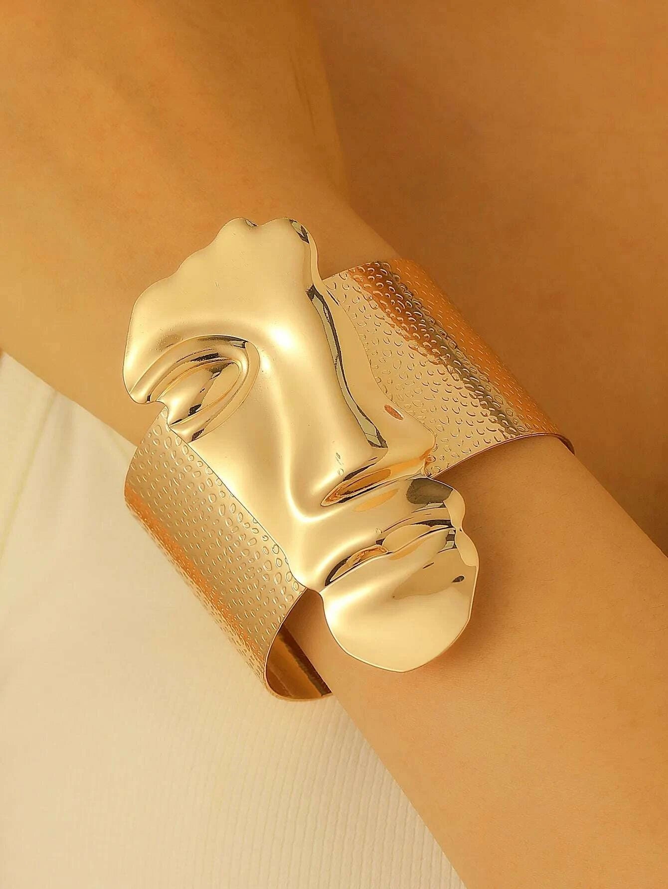 Gold face-shaped cuff bracelet on a wrist against a neutral background