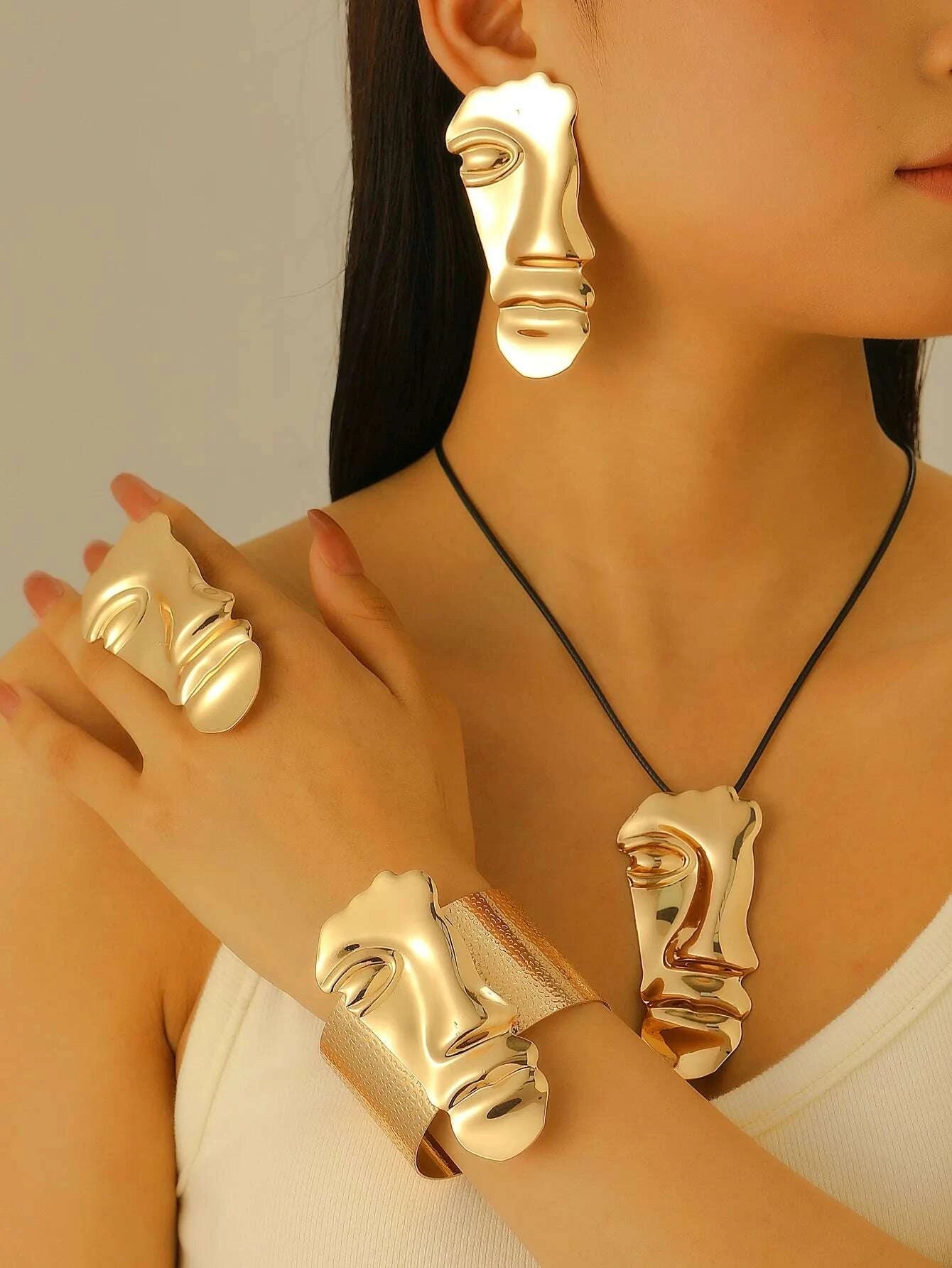 Gold face-shaped jewelry set including earrings, bracelet, and ring on a neutral background