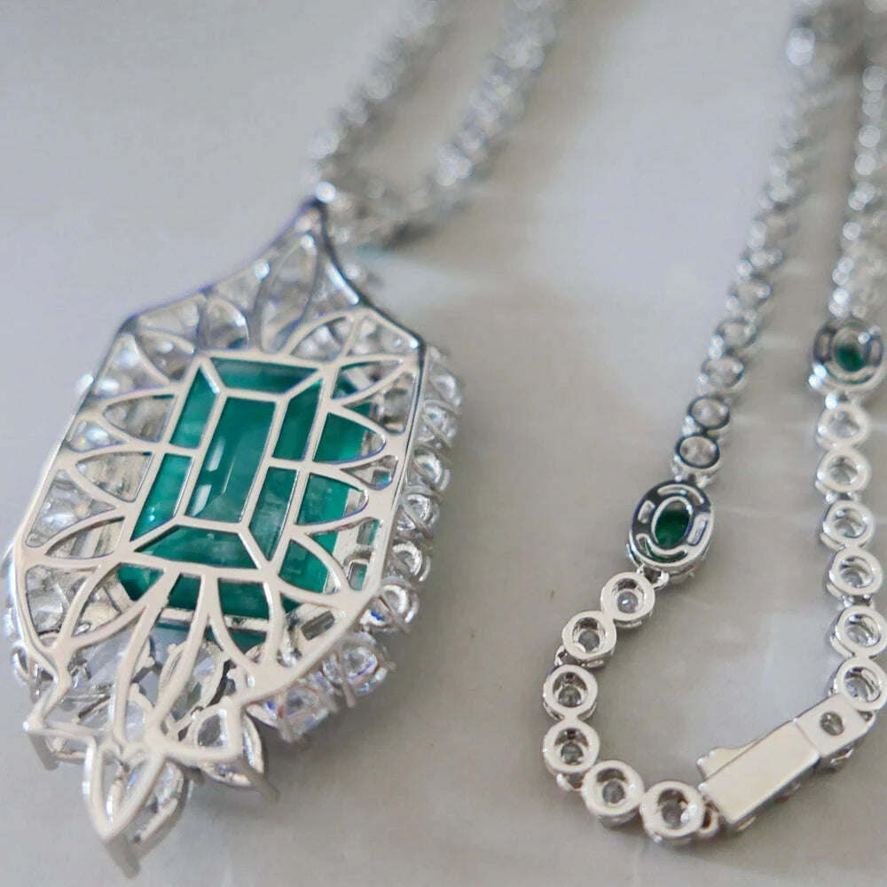 Silver filigree pendant necklace featuring a geometric emerald-cut green gemstone centerpiece, shown on a light neutral background.