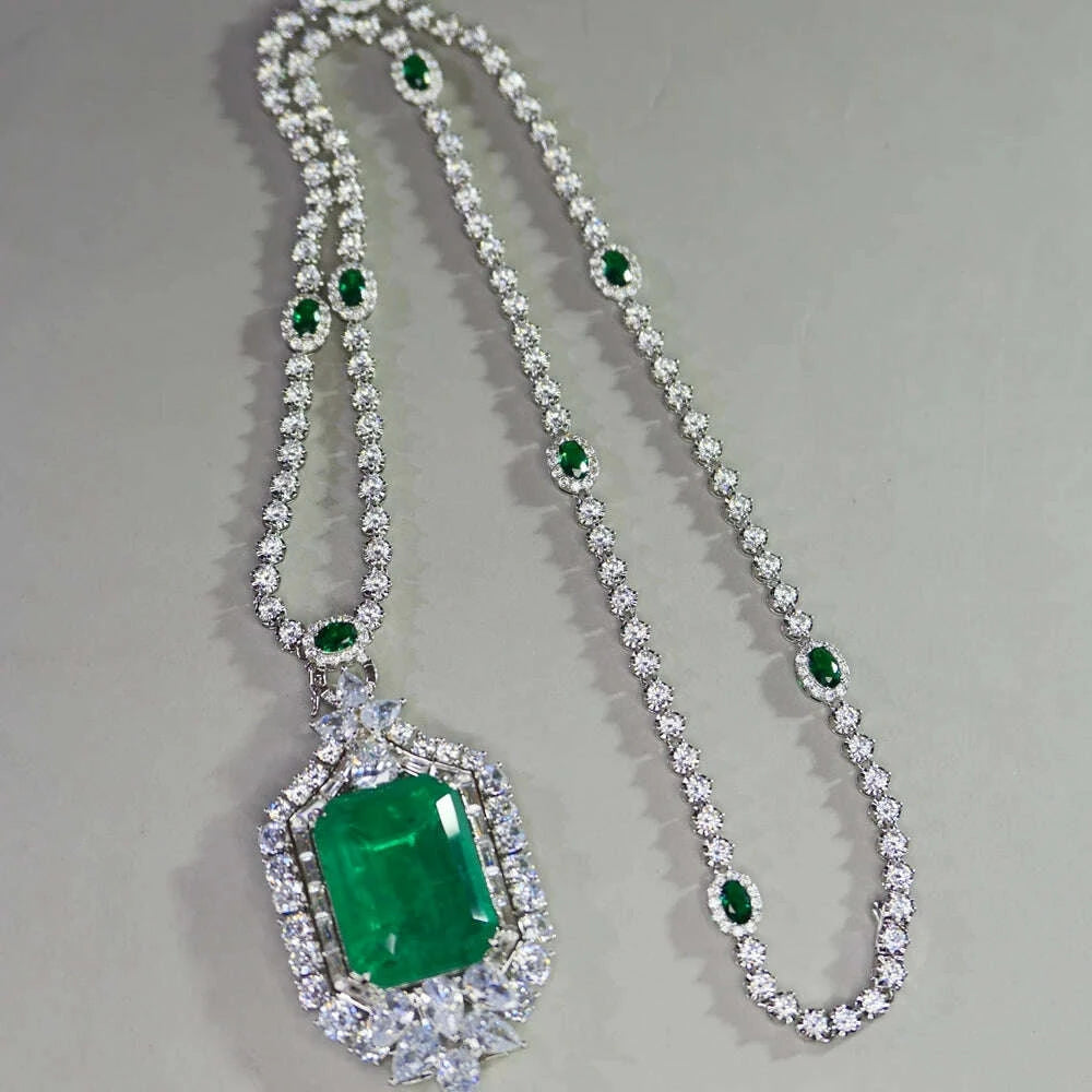 A silver-toned double-strand necklace featuring a large rectangular emerald-cut green gemstone pendant surrounded by clear stones, with smaller green gemstone accents along the chain.